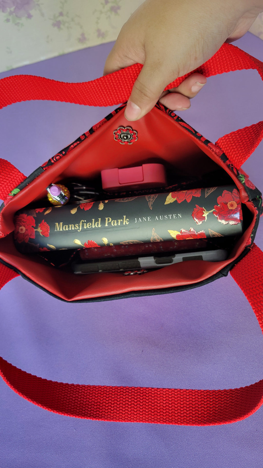 A Red Toe bag called Tracy style with two straps in red. The 5 quilt style bag has the color black., red with black polka dots, red swirls and hearts in black background, and red roses with green leaves pattern on background fabric. 

Inside of the purse is items it can fit. A hand sanitizer, a red heart wallet, an example book it can fit, a touch phone and Ursula pen.

There is only one with a closure of a vintage flower push bottom