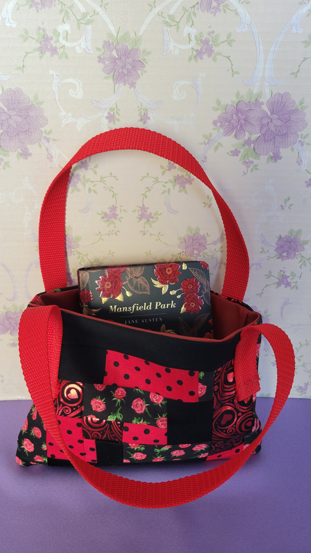 A Red Toe bag called Tracy style with two straps in red. The 5 quilt style bag has the color black., red with black polka dots, red swirls and hearts in black background, and red roses with green leaves pattern on background fabric. 

Inside of the purse is an example book of Manfeild Park.