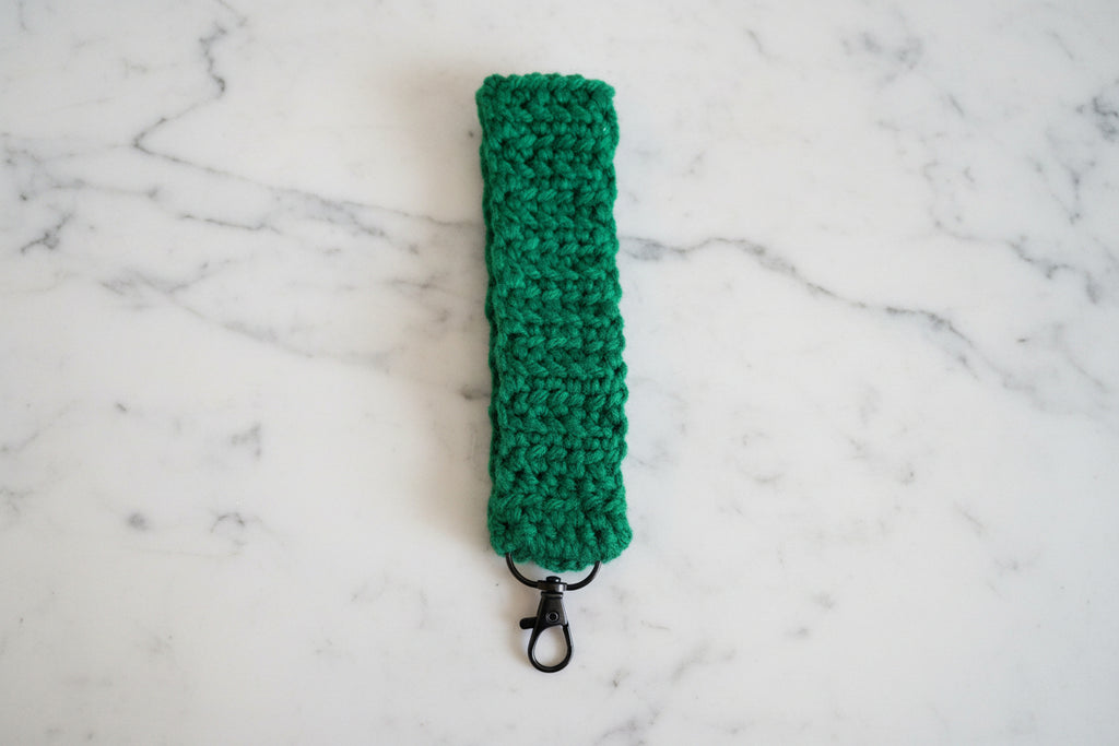 Green crochet bracelet on a wrist with a marble background. 