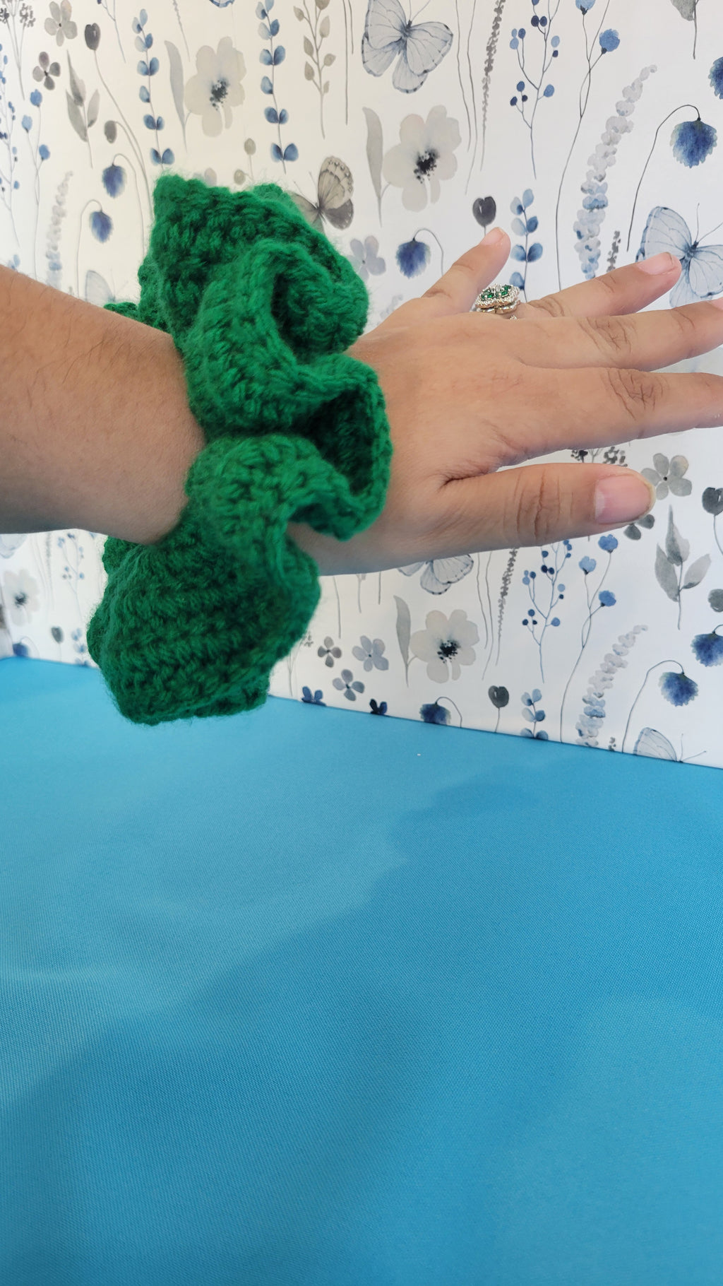Green crochet scrunchie on a hand with a patterned fabric background