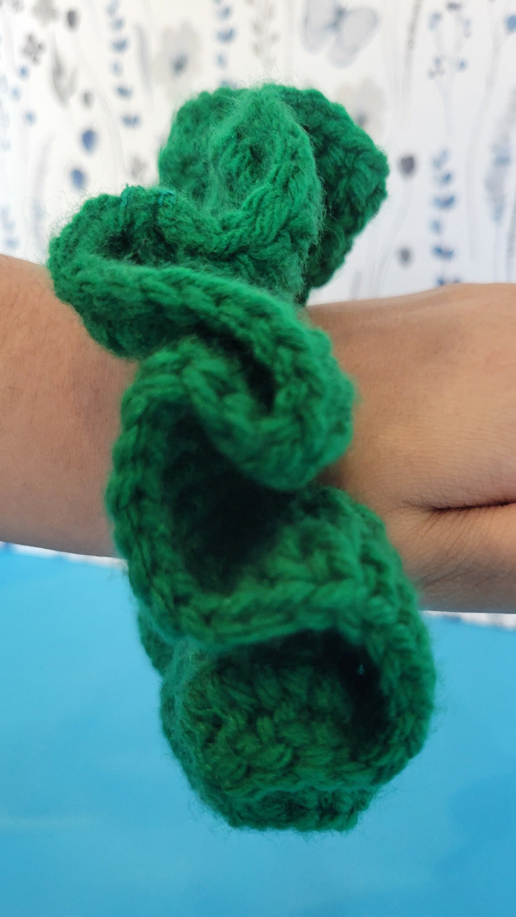Green crochet scrunchie on a wrist with a blurred background