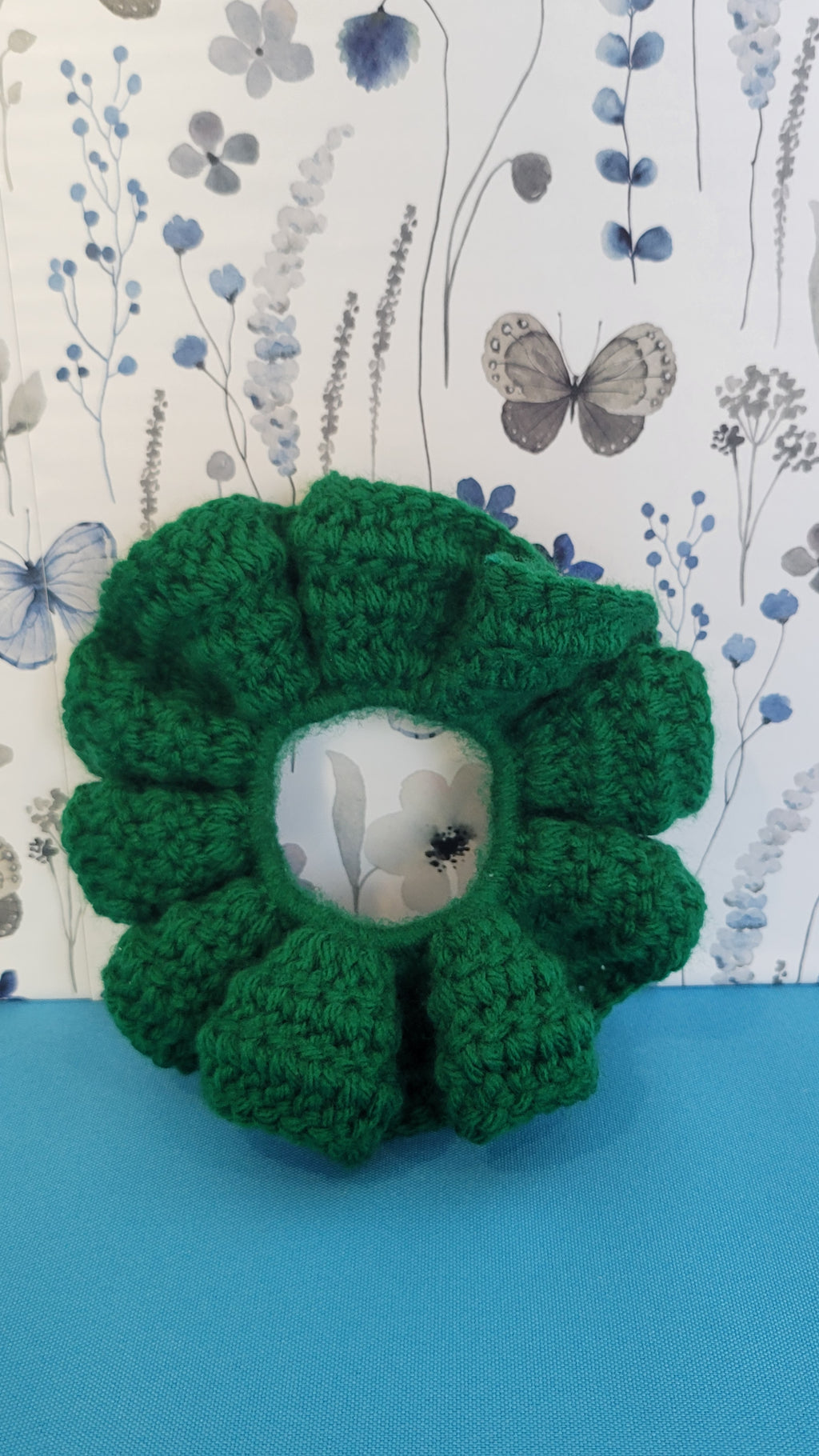 Green crocheted scrunchie on a floral design background.