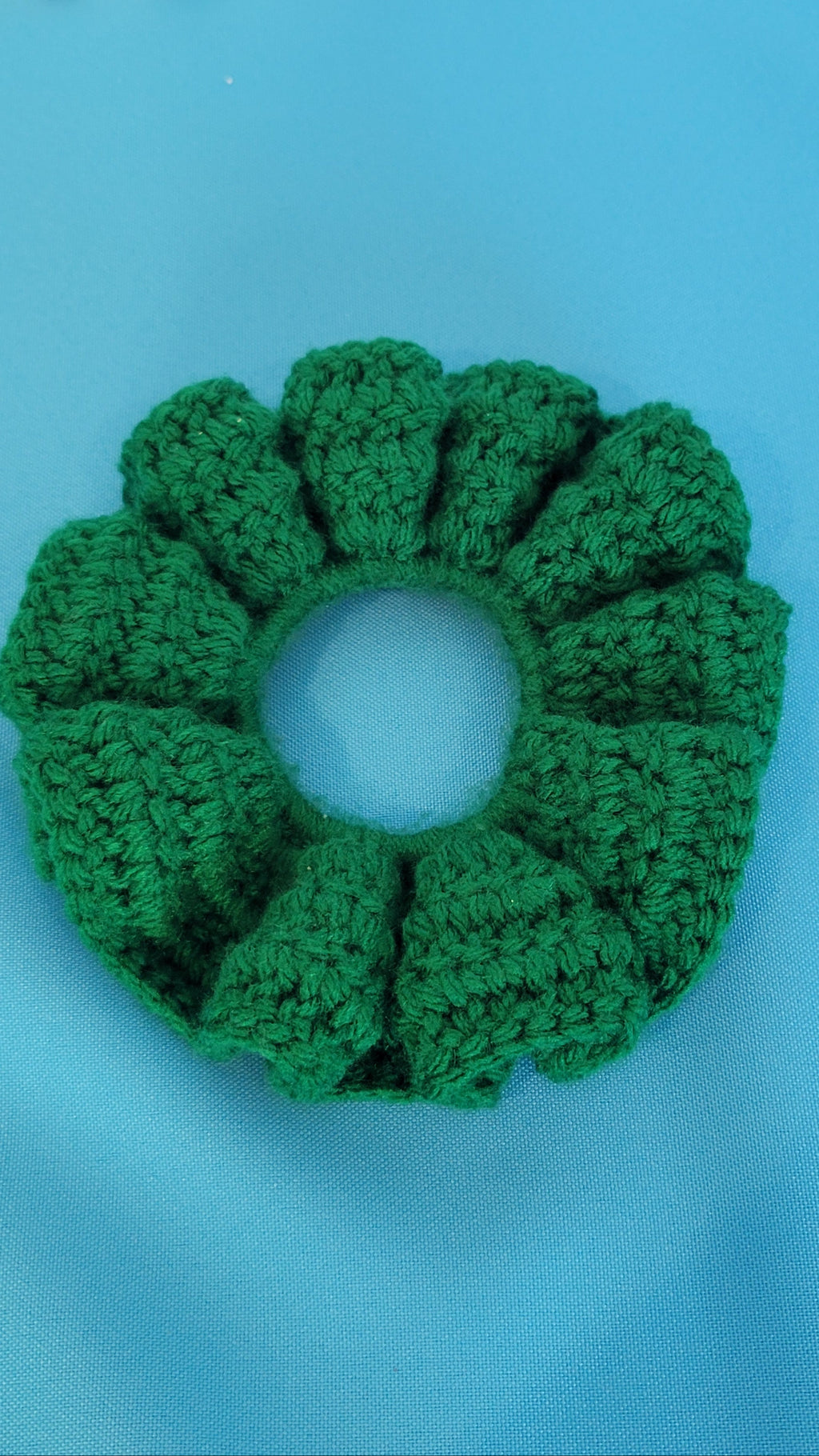 Green crocheted scrunchie on a blue background
