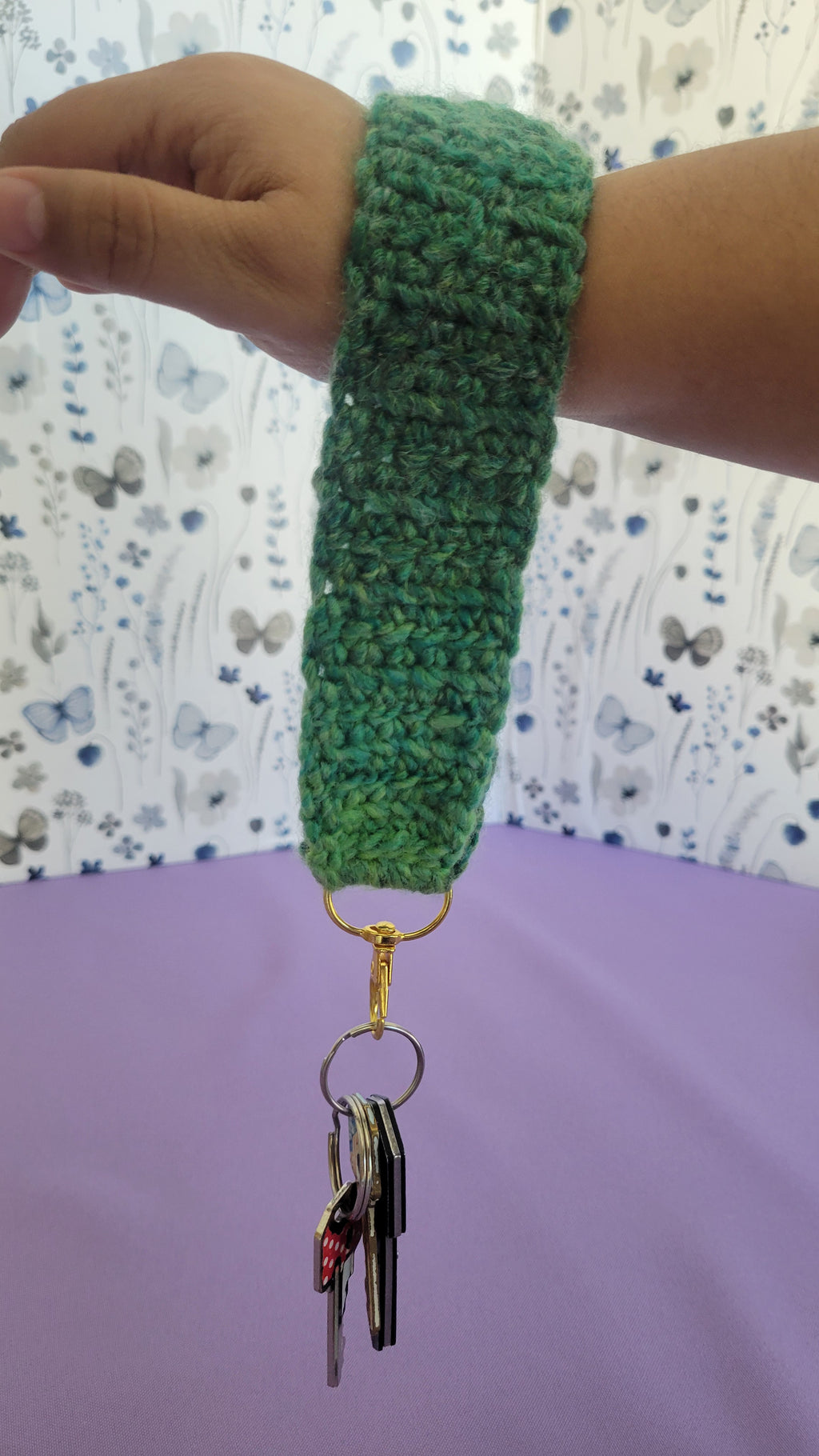 Green crochet key bracelet item with a key attached, held by a person against a textured background. The size of the bracelet is seven inches.