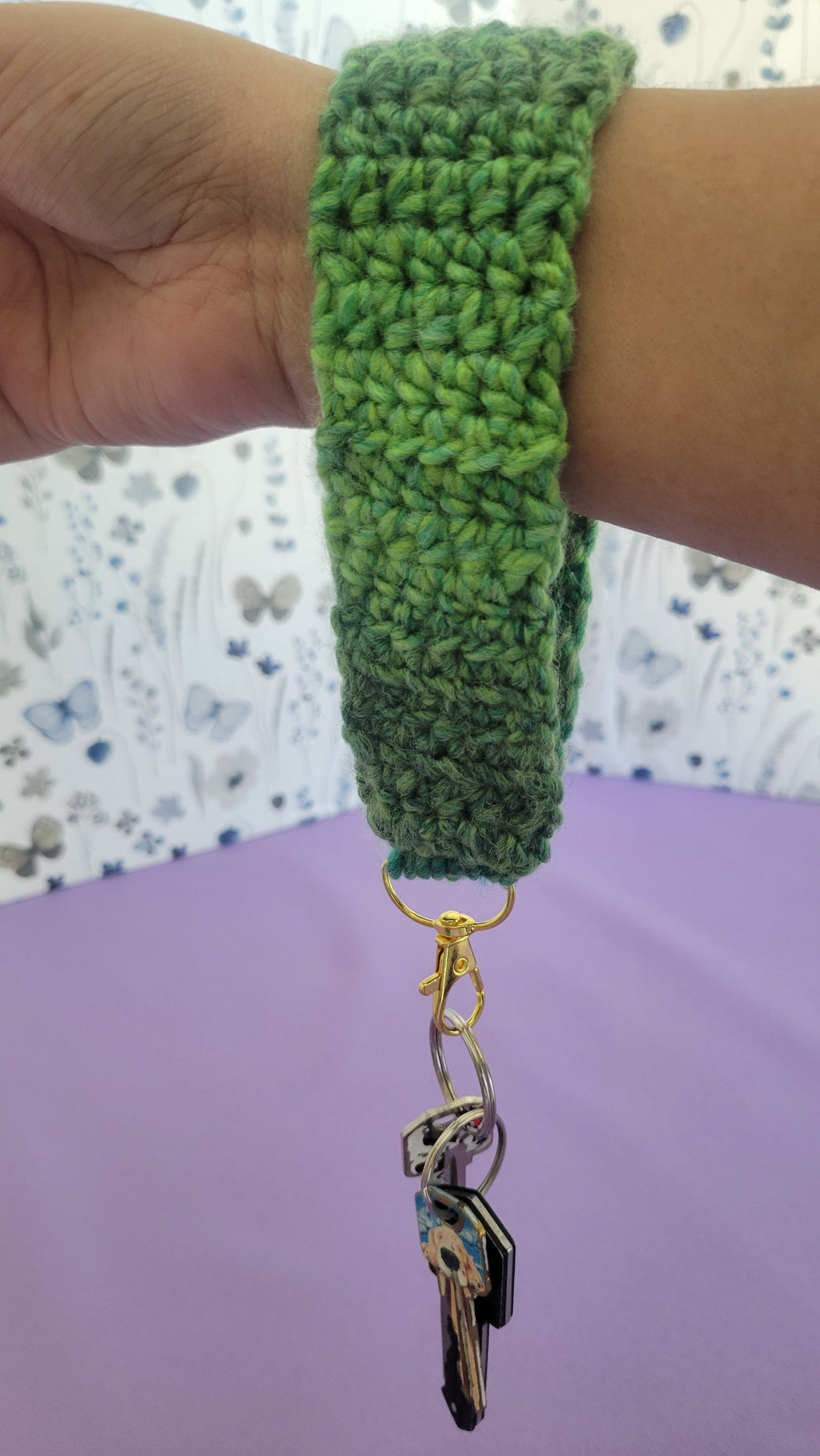 Green crochet key bracelet item with a key attached, held by a person against a textured background. The size of the bracelet is six in inches.