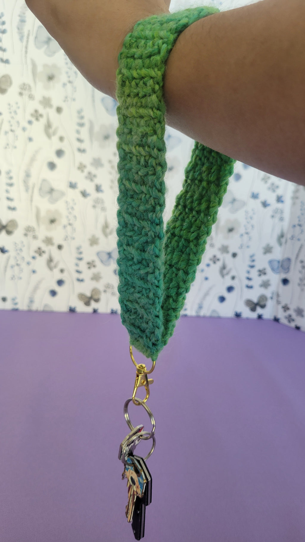 Green crochet key bracelet item with a key attached, held by a person against a textured background. The size of the bracelet is 8 in inches.
