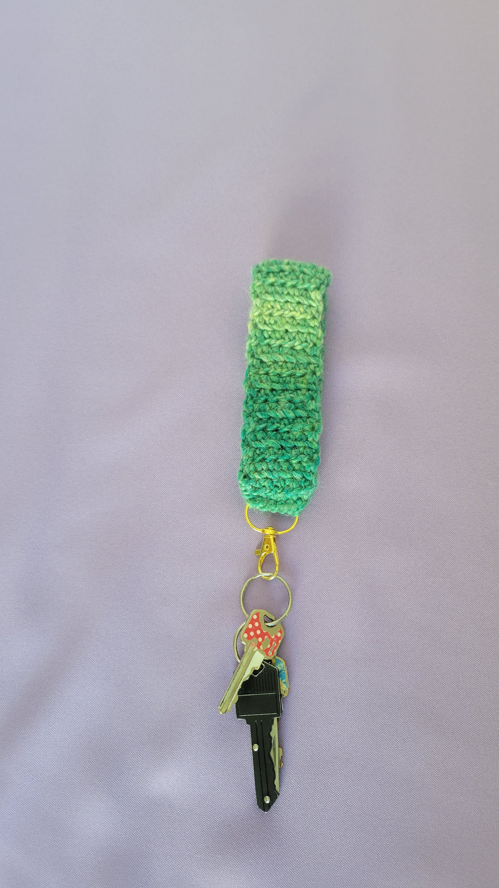 Green crochet key bracelet item with a key attached,against a purple background. The size of the bracelet is 5 inches.