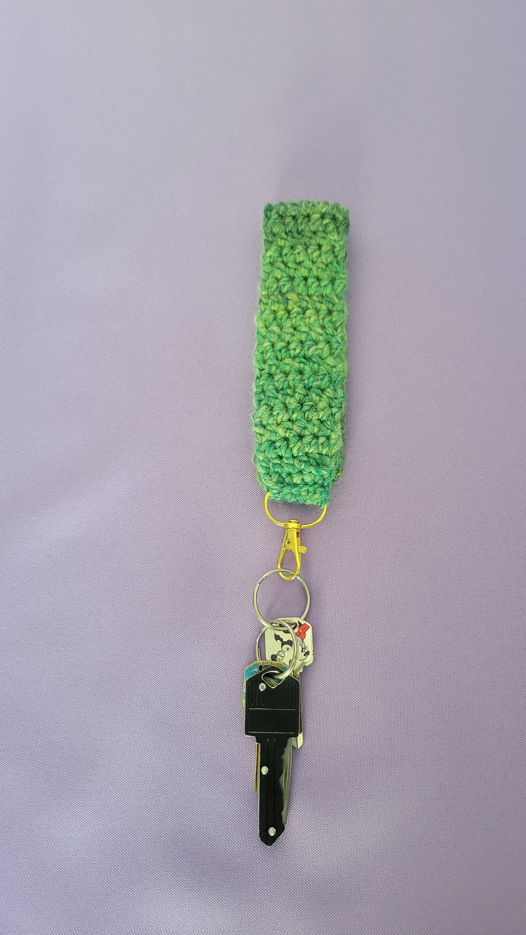 Green crochet key bracelet item with a key attached,against a purple background. The size of the bracelet is six inches.