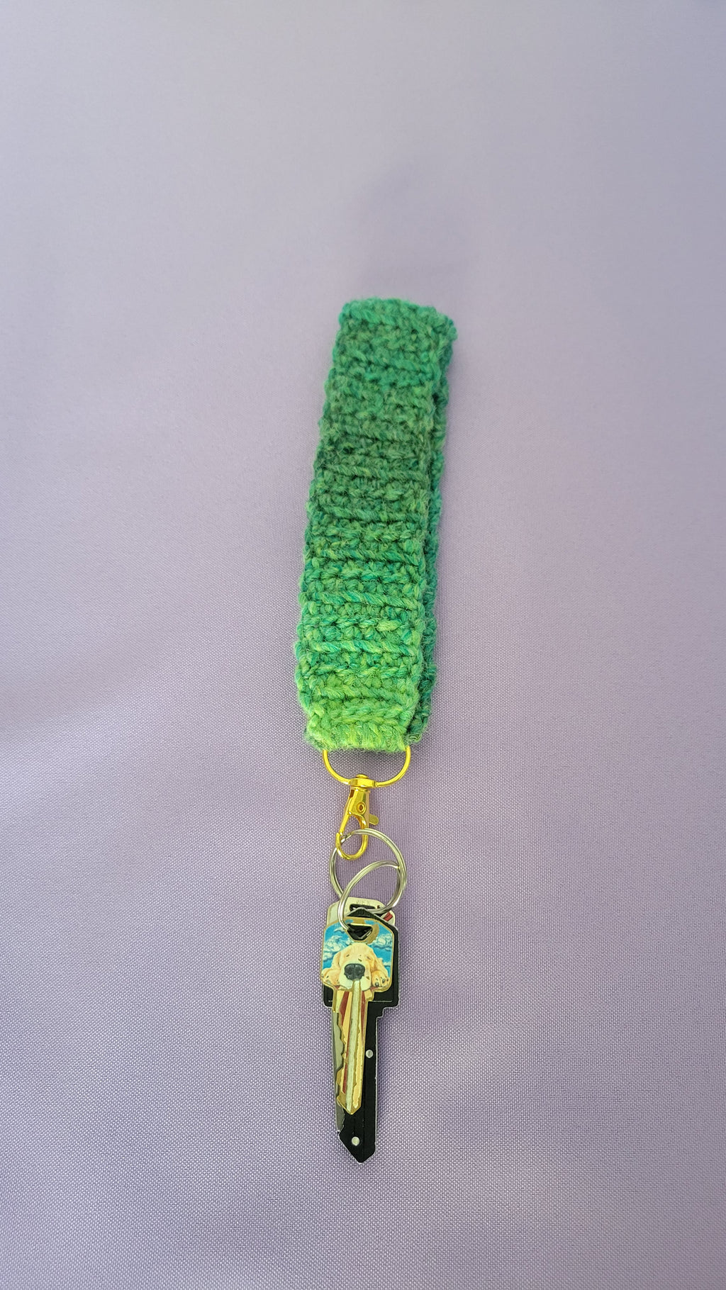 Green crochet key bracelet item with a key attached,against a purple background. The size of the bracelet is seven inches.