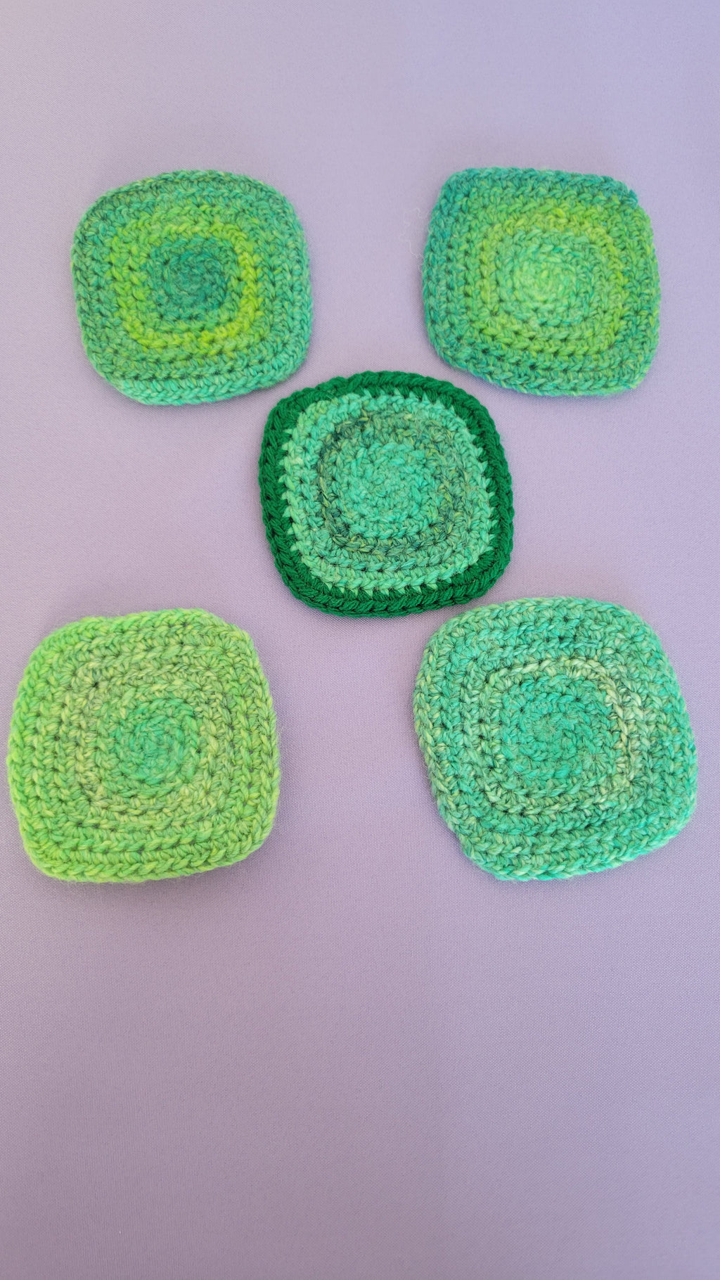 Five green crocheted coasters on a purple surface.