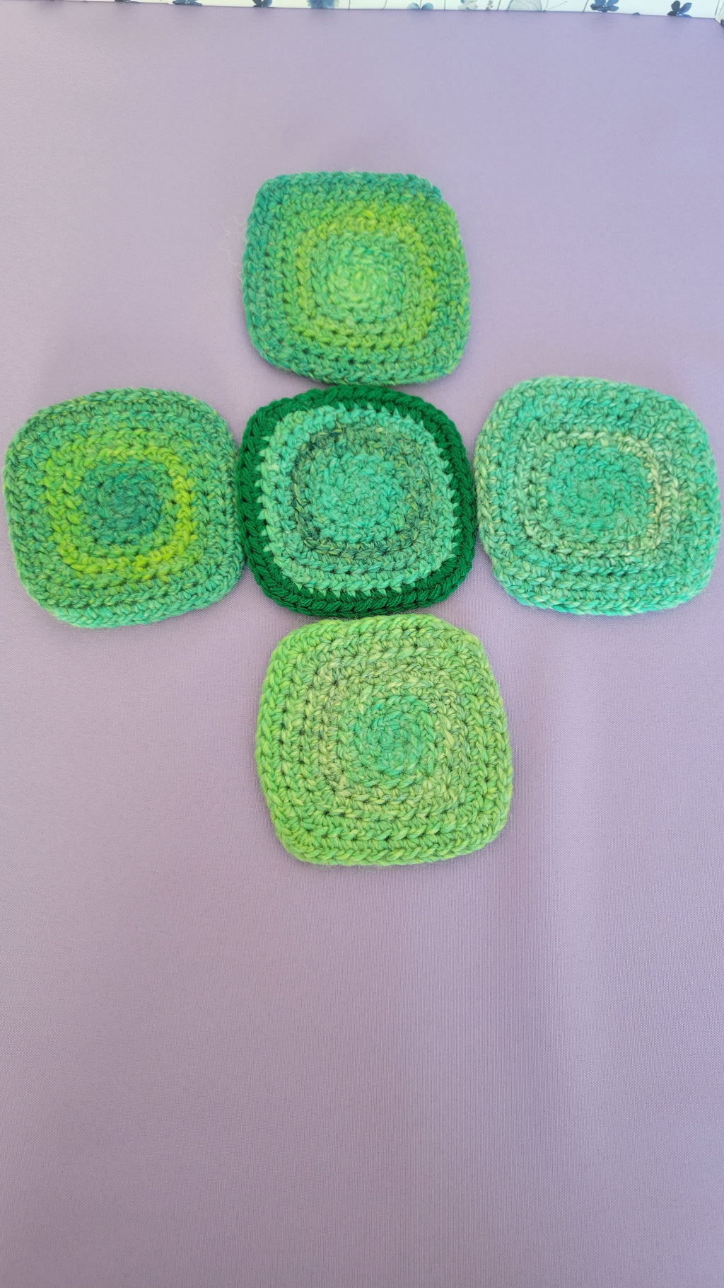 Five green crocheted coasters on a purple surface.