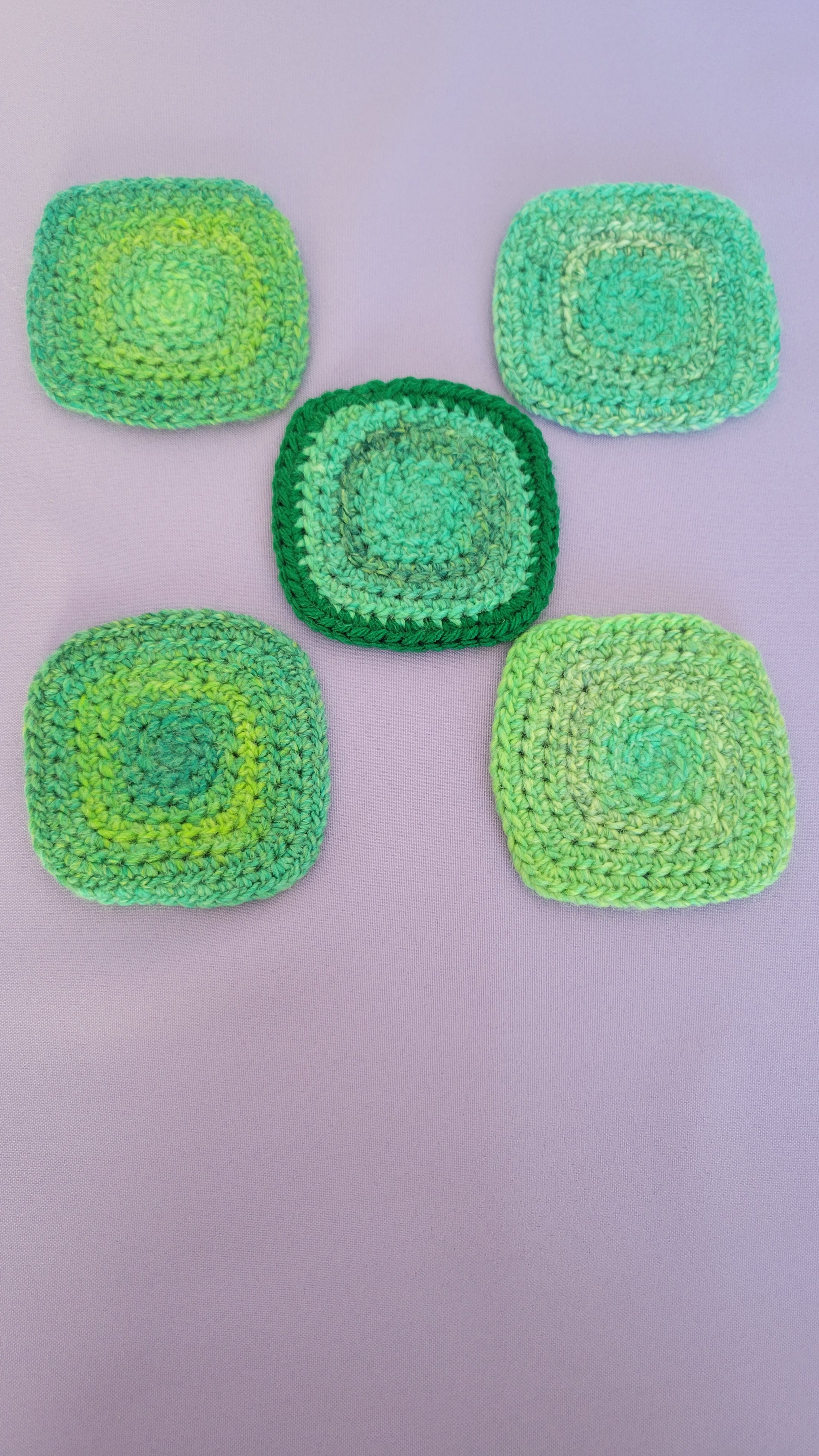 Five green crocheted coasters on a purple surface.