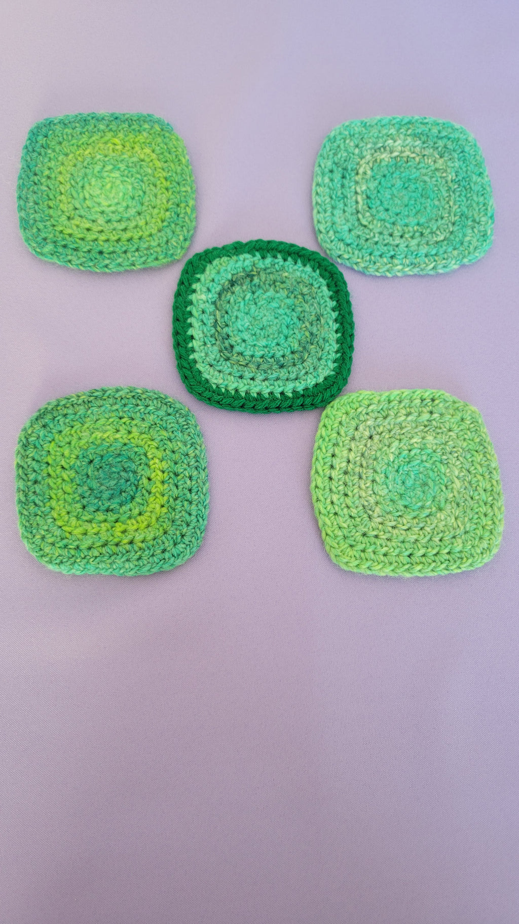 Five green crocheted coasters on a purple surface.