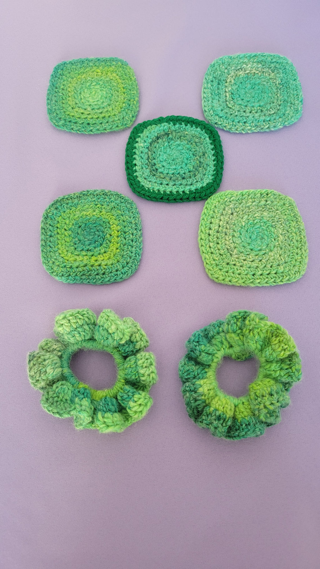Five green crocheted coasters and a pair of scrunchies on a purple surface.